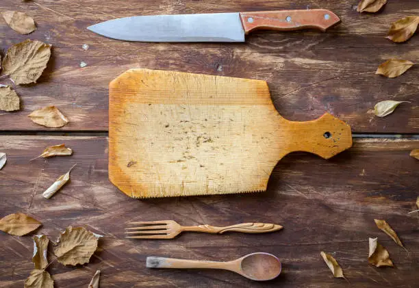 Wooden kitchen board, wooden spoon and fork, kitchen knife, on an old wooden table. Top view. Copy space
