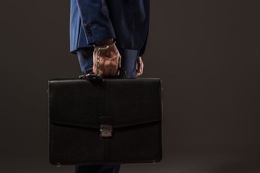 side view of businessman in handcuffs holding briefcase isolated on black