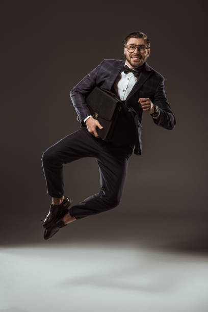 istock excited businessman with briefcase jumping and looking at camera on black 997592476