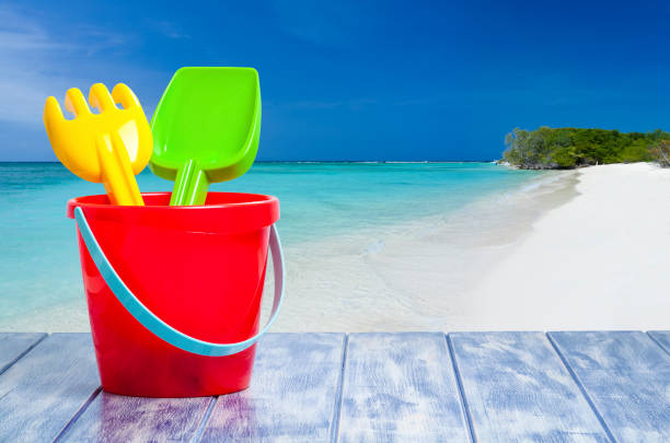 Sand pail and shovel shot against turquoise colored beach background. The Objects are on a blue colored plank and grouped at the left of an horizontal frame leaving useful copy space for text and/or logo at the center-right. Predominant colors are blue and red. DSRL photo taken with Canon EOS 5D Mk II and Canon EF 100mm f/2.8L Macro IS USM.