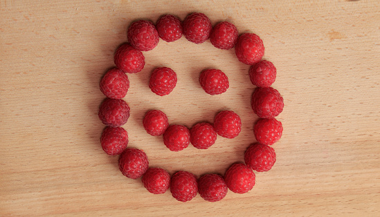 Smiling face laid out of ripe raspberries on a wooden cutting board
