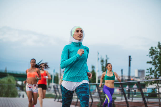 Determined to win Multi ethnic group of young  women exercise outdoor, next to the river. They are wearing sport clothing, running, stretching, celebrate and support each other. marathon stock pictures, royalty-free photos & images