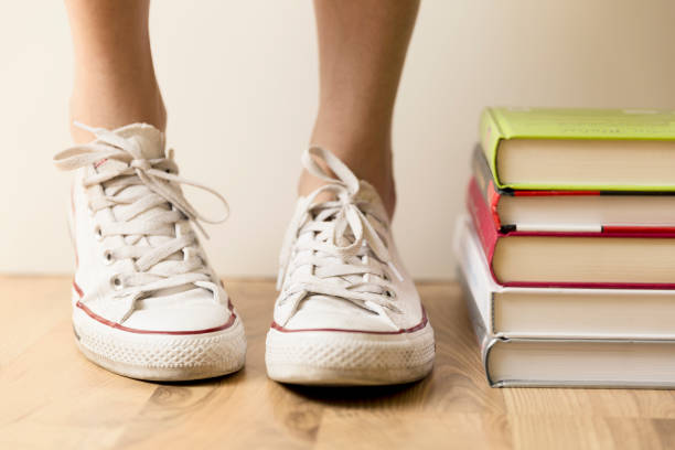 White sneakers and stack of books on the floor. Student, education and knowledge concept