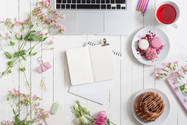 istock Feminine flat lay workspace with laptop, cup of tea, planner, macarons and flowers on white wooden table. Top view mock up. 997660318