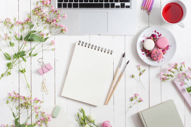 istock Feminine flat lay workspace with laptop, cup of tea, macarons, flowers, notebook, brushes, on white wooden table. Top view mock up. 997660440