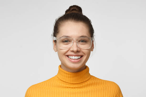 微笑し、笑う黄色のタートルネックのセーターと灰色の背景に分離した透明な眼鏡の魅力的な若い女性のショットを閉じる - close up women horizontal citrus fruit ストックフォトと画像