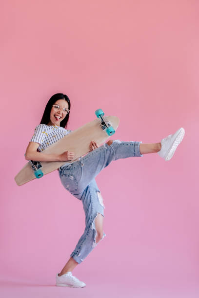Young girl on pink background Young asian teenage girl on pink background. Stylish young woman with skateboard isolated. hipster fashion stock pictures, royalty-free photos & images