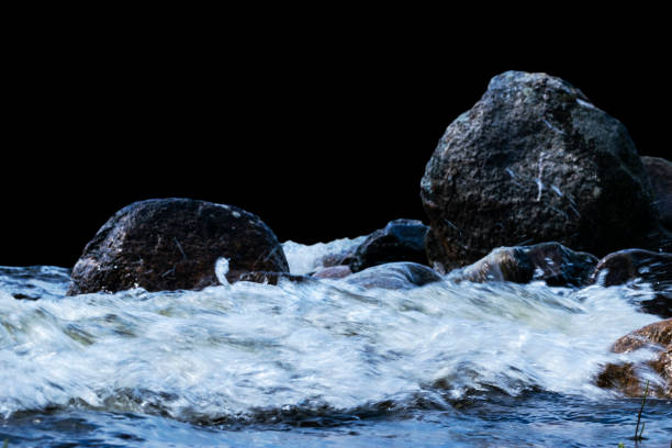 istock Big windy waves splashing over rocks. Wave splash in the lake isolated on black background. Waves breaking on a stony beach, forming a spray. Water splashes. Water surface texture 997665976