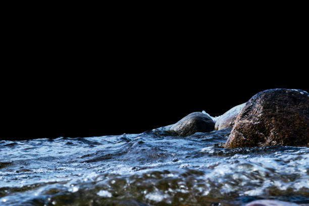 istock Big windy waves splashing over rocks. Wave splash in the lake isolated on black background. Waves breaking on a stony beach, forming a spray. Water splashes. Water surface texture 997666048