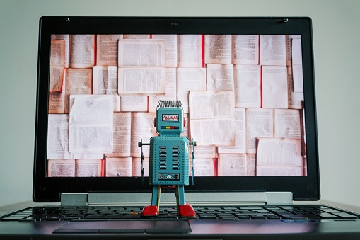 Robots looking at laptop screen with open books, artificial intelligence, big data and deep learning concept