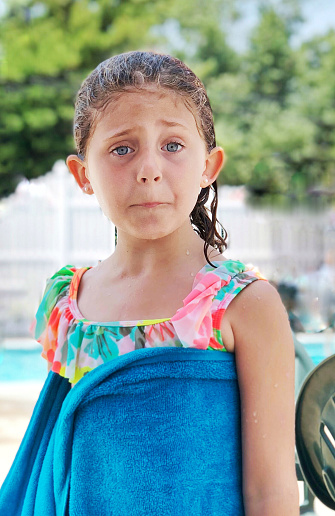 Six year old gril who is unhappy standing near a swimming pool