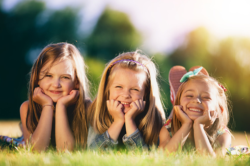 Three smiling little girls laying on the grass in the park. Childhood friendship. Sisterhood.