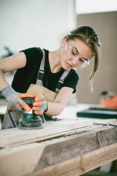 istock Female Carpenter Apprentice Preparing Wooden Block For Further Use 997679372