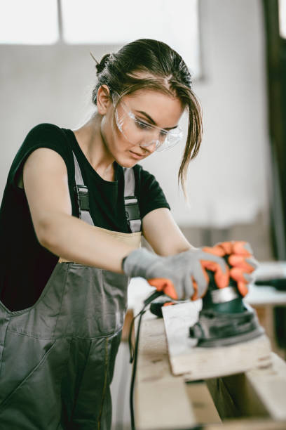 istock Cute Female Carpenter Sanding Wood In Workshop 997679408