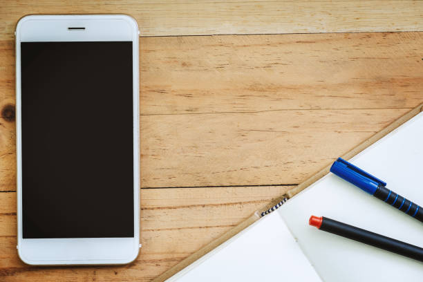 istock Smartphone, an opened notebook and pens on wooden table background for business and technology concept 997685328