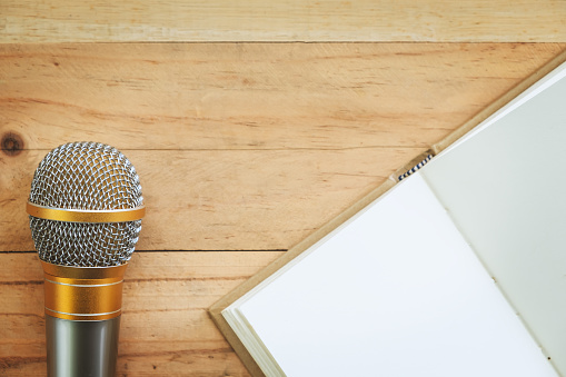 Microphone and opened notebook on wooden background for speaking, learning and teaching concept