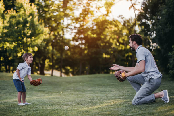 Dad with son playing baseball Handsome dad with his little cute sun are playing baseball on green grassy lawn baseball sport photos stock pictures, royalty-free photos & images