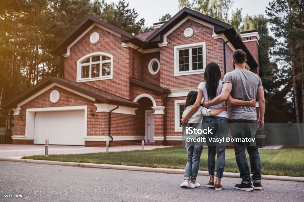 Happy family outdoors Back view of happy family is standing near their modern house and hugging House Stock Photo