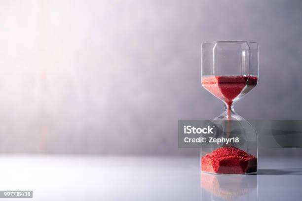 Red Sand Running Through The Shape Of Modern Hourglass On White Tabletime Passing And Running Out Of Time Urgency Countdown Timer For Business Deadline Concept With Copy Space Stock Photo - Download Image Now