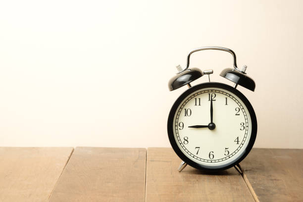 black vintage alarm clock close to the window present nine o'clock