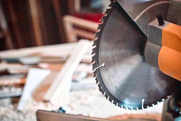 Closeup of a circular saw in a carpentry workshop against a background of wooden scraps and blanks.