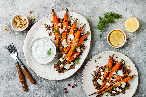 Roasted carrots lentil salad with feta, herb yogurt and dukkah on a light concrete background. Vegetarian food. Top view, flat lay