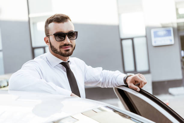 istock handsome driver in sunglasses standing near car and looking at camera 997768488