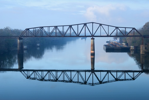 Looking down river at old railroad train truss bridge reflecting in foggy water