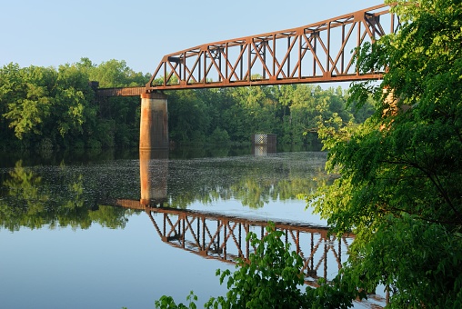 Looking up at old rusty railroad train bridge crossing river with reflection