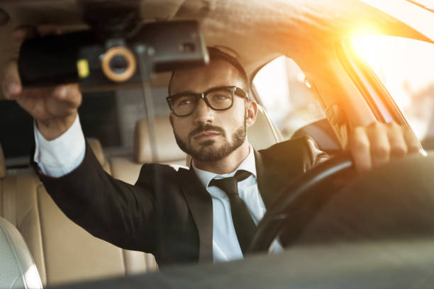 istock handsome driver in suit driving car and fixing mirror during sunset 997778004