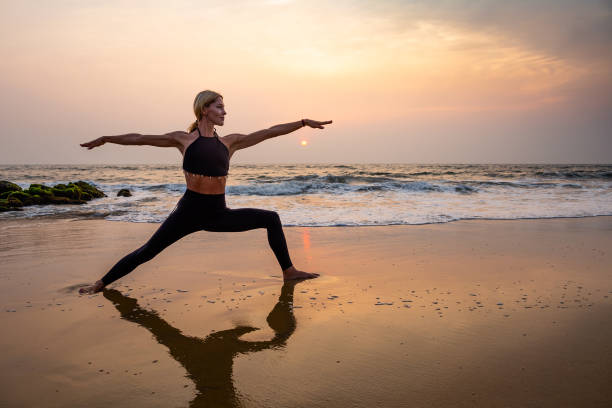 Middle age woman in black doing yoga on sand beach in India Middle age woman in black doing yoga on sand beach in India  standing asana virabhadrasana at sunset. Healthy lifestyle. warrior position stock pictures, royalty-free photos & images