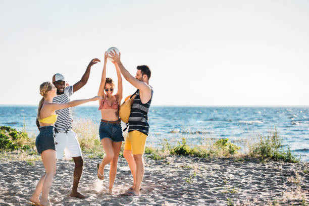 istock happy young multiethnic friends holding ball on sandy beach 997812072
