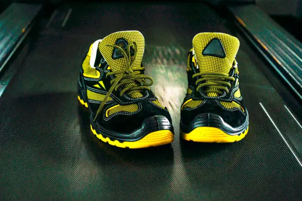 Unbranded modern sneaker in the gym. Black-Yellow. Comfortable shoes. Wearing sport shoes, doing wide step, demonstrating healthy way of life, wide shot. copy space for text.