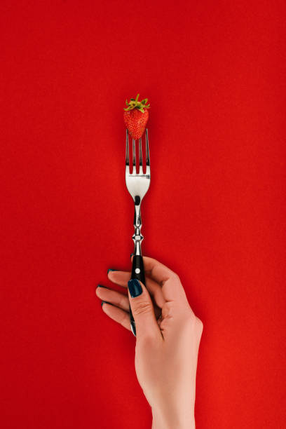 istock Female hand holding fork with strawberry isolated on red background 997835278