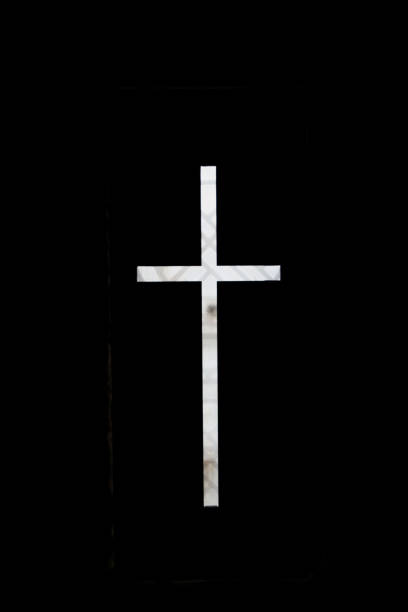A black and white photo of a white marble church cross standing out against black background