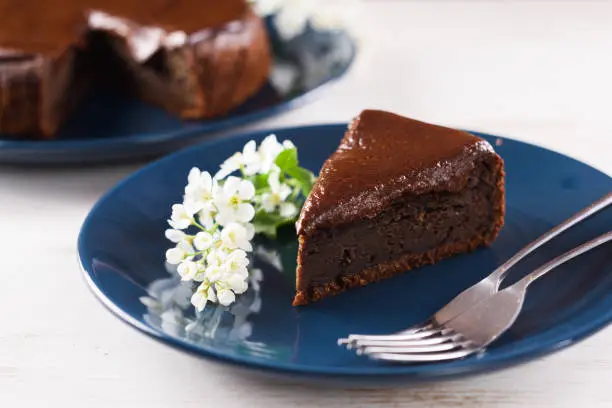 Healthy homemade dessert. Piece of bird cherry chocolate cake decorated with bird cherry flowers on navy blue plate closeup