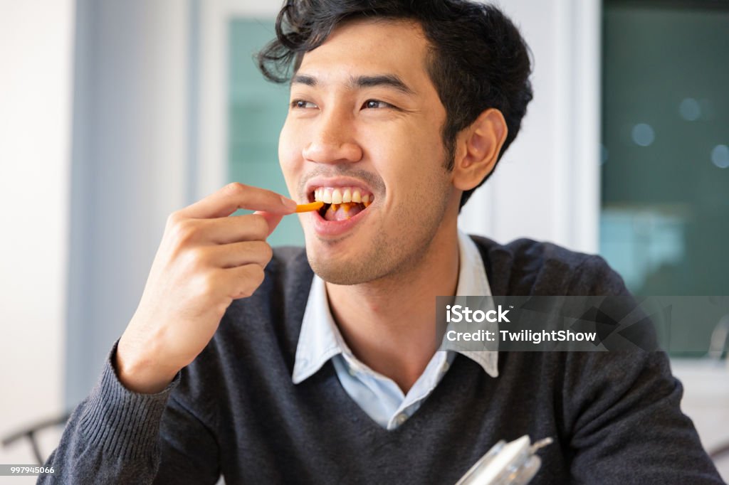 One young college students adult male taking a break sat eating snack with happiness Young college students adult male sat eating snack with happiness in room Snack Stock Photo