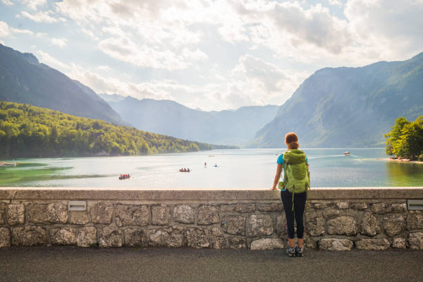 jovem mulher usando mochila verde está de pé sobre a ponte perto do lago bohinj olhando a vista em bohinj, eslovénia - bohinj - fotografias e filmes do acervo