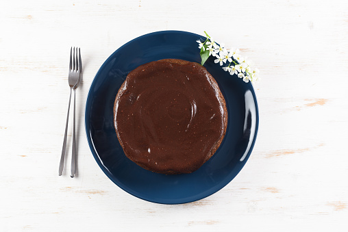 Healthy homemade dessert. Bird cherry cake with chocolate icing decorated with bird cherry flowers in blue plate on white background copyspace overhead view