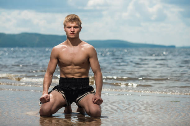 A man meditates on the beach in sea background after a workout.