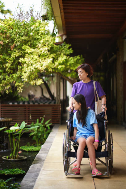 menina asiática lesada, sentado em uma cadeira de rodas e a mãe dela - welfare cuts - fotografias e filmes do acervo
