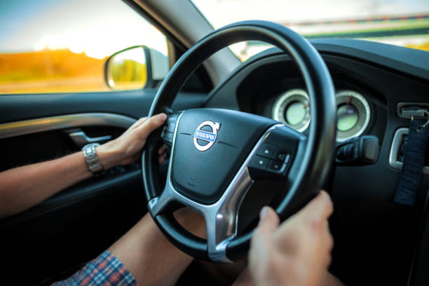 Driver in shorts holds a Volvo steering wheel during car ride on freeway. Berlin / Germany - April 29, 2018: Driver in shorts holds a Volvo steering wheel during car ride on freeway. volvo photos stock pictures, royalty-free photos & images