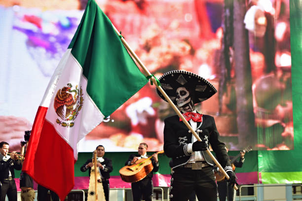 Moscow, Russia - June 29, 2018: Man in hat with sugar skull makeup waving mexican flag during Dia de los Muertos Mexican parade. Day of The Dead