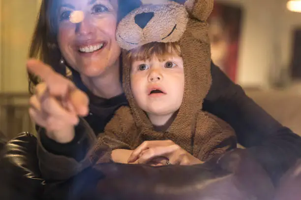 Photo of Baby Boy inside Bear Costume Looking Trough Window with Mom