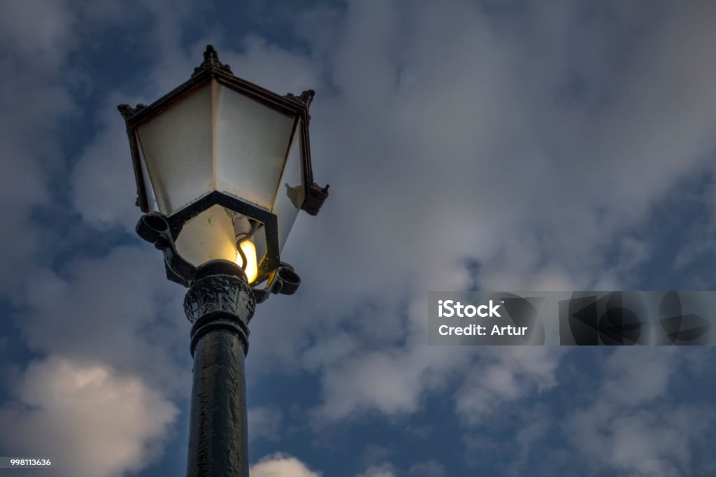 An Incandescent Bulb With A Broken Glass Glowing In An Antique Street Lamp Postthe Medieval European Lamp Is Made Of Cast Steel Is Made Of An Ornate Top Stock Photo -