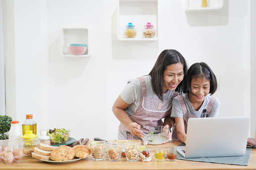 Mother and daughter learn cooking using laptop computer in the kitchen at home, happy family asian concept