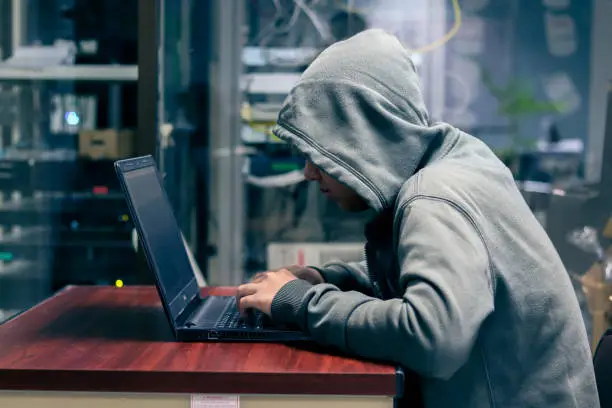 Photo of Hacker is Using Computer for Organizing Massive Data Breach Attack on Corporate Servers. Their Hideout is Dark