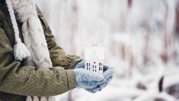 Female hands holding tiny home in snowy weather