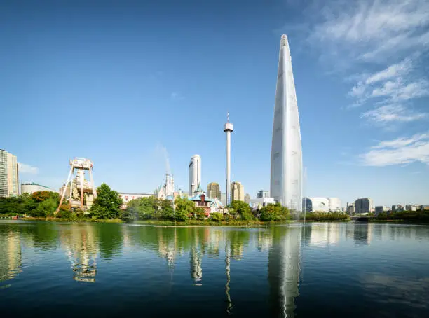 Beautiful view of lake and park at downtown of Seoul, South Korea. Skyscraper is visible on blue sky background. Scenic sunny cityscape. Modern buildings reflected in water.
