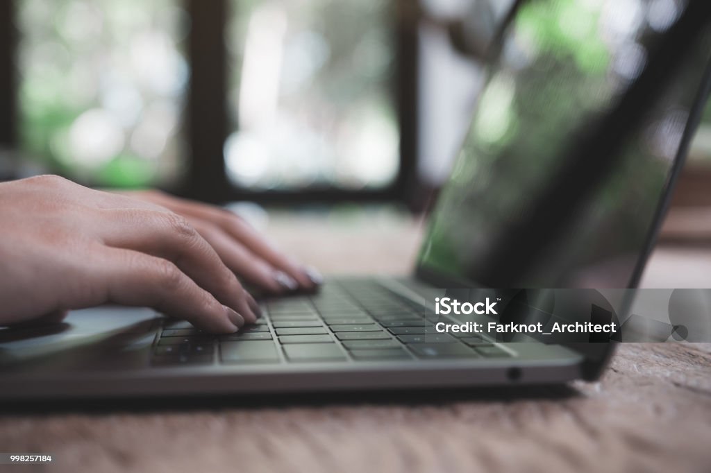 Closeup image of a woman's hands working and typing on laptop keyboard on wooden table Adult Stock Photo